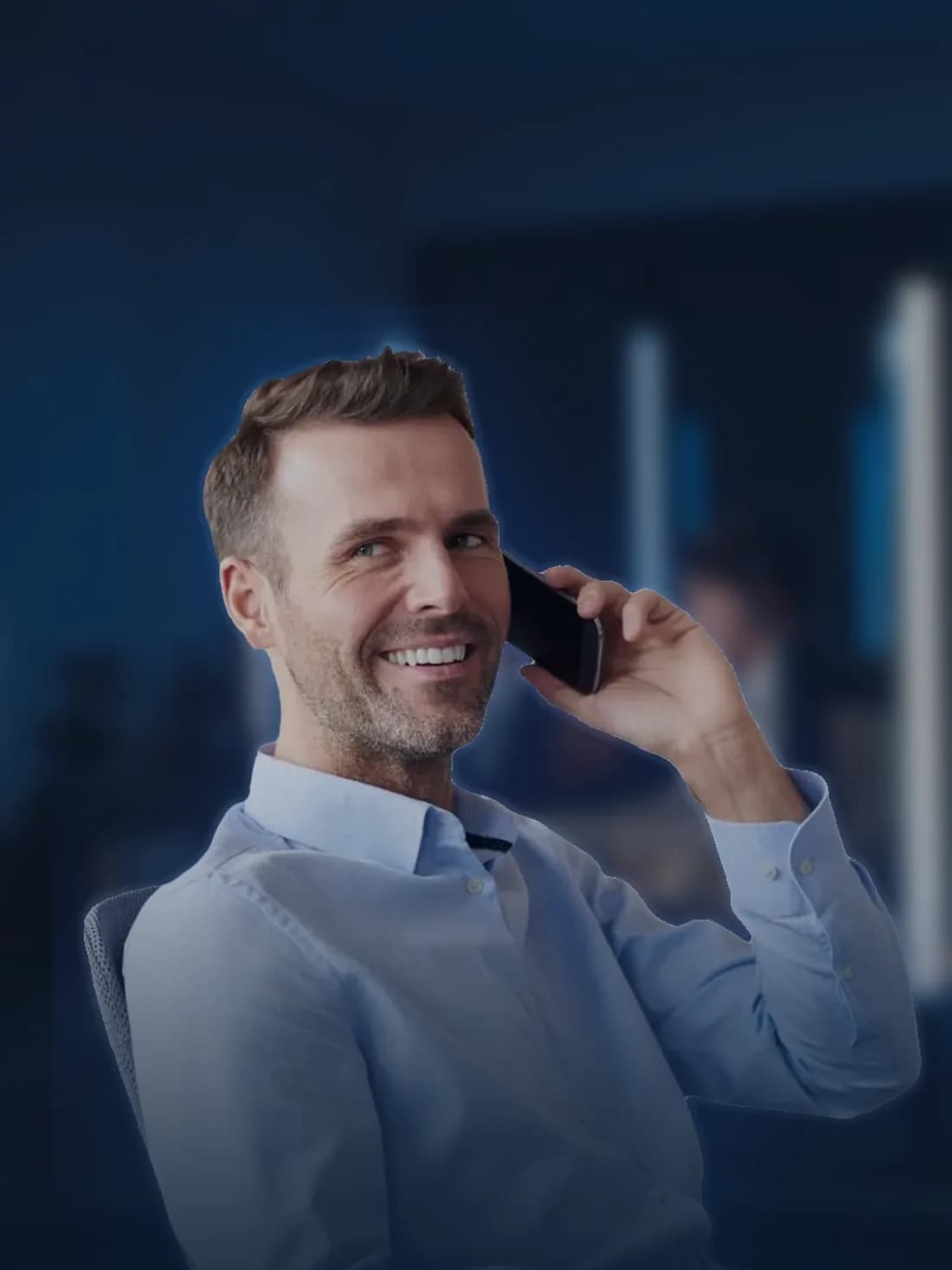 Un homme souriant, au téléphone, assis dans un bureau en soirée.